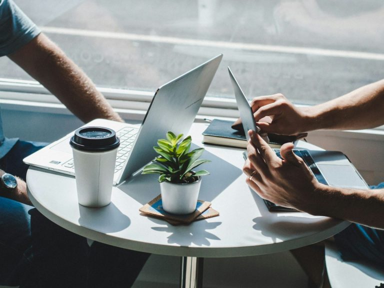 Two people sit at a bistro table exchanging ideas over computers and coffee.
