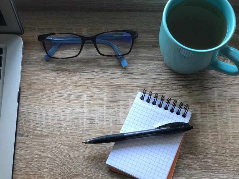 A pair of glasses, a cup of tea and a notebook to take notes on what a client needs.